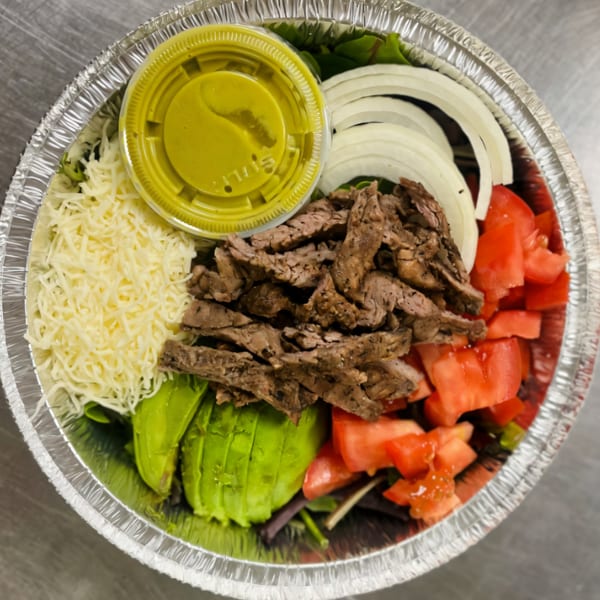 Dona Mary's Mexican steak salad with avocado, tomatoes, onions, cheese, and green dressing in a foil container.
