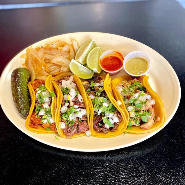 Four Dona Mary tacos with various fillings, cilantro, onions, lime, grilled onions, and sauces.