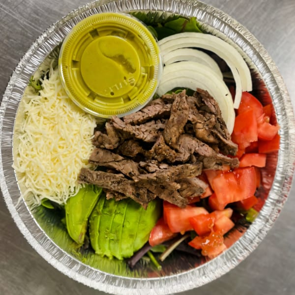 Dona Mary's Mexican steak salad with avocado, tomatoes, onions, cheese, and green dressing in a foil container.