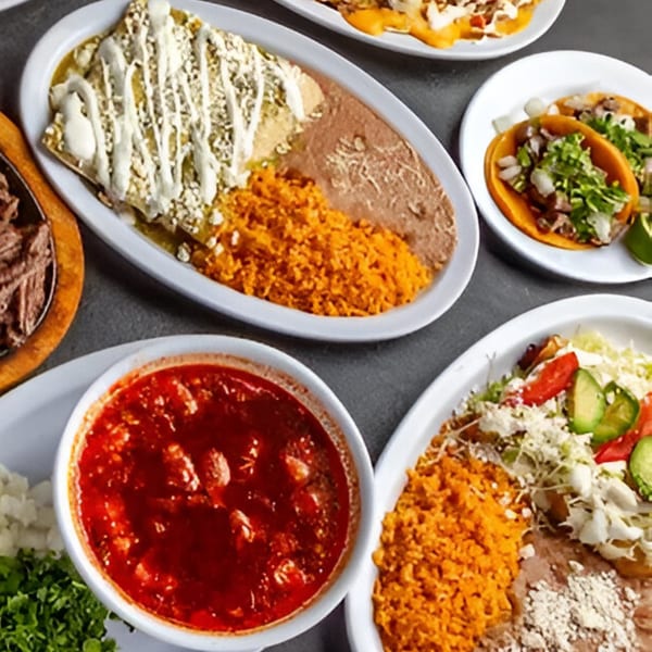 A Dona Mary Mexican feast with enchiladas, tacos, rice, beans, and salsa on a dark table.
