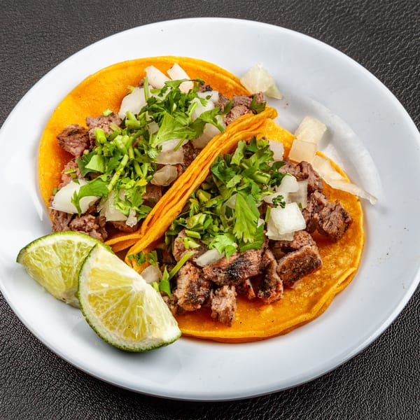 Two Dona Mary carne asada tacos with cilantro, onions, and lime wedges on a white plate.