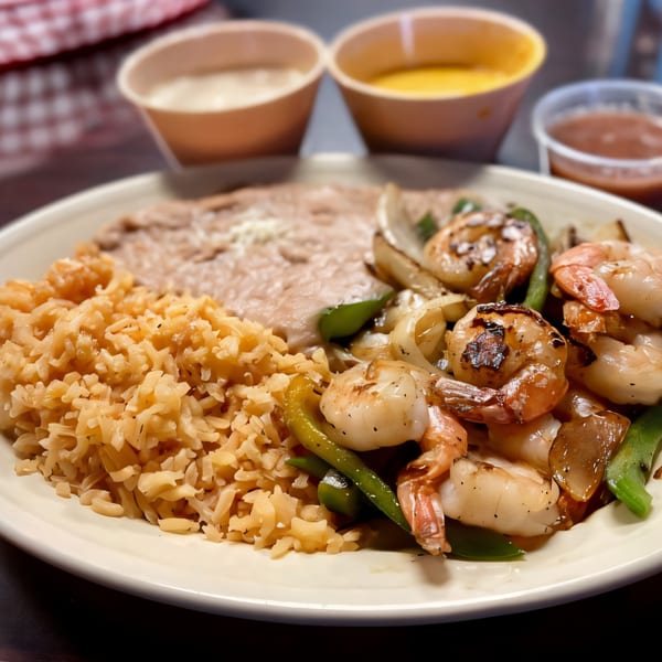 A plate of Dona Mary's Mexican shrimp fajitas with rice, refried beans, and dipping sauces.