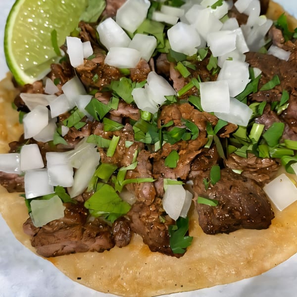 Dona Mary's carne asada taco with diced onions, cilantro, and a lime wedge.