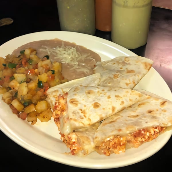 Dona Mary's Mexican plate with quesadillas, refried beans, and diced potatoes, with salsa bottles in the background.
