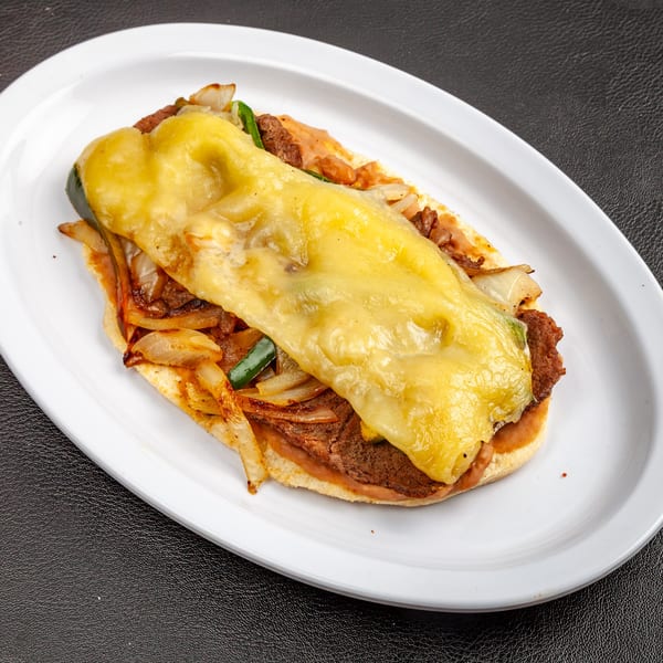 Dona Mary's Mexican torta with melted cheese, meat, onions, and green peppers on a white plate.