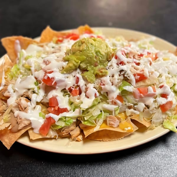Dona Mary's chicken nachos, topped with guacamole, sour cream, lettuce, tomatoes, and shredded cheese.