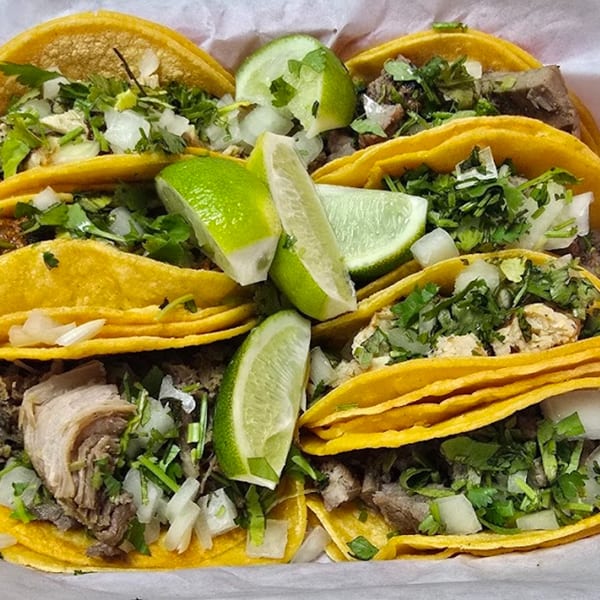 A close-up of several Dona Mary Mexican tacos with meat, cilantro, onions, and lime wedges.