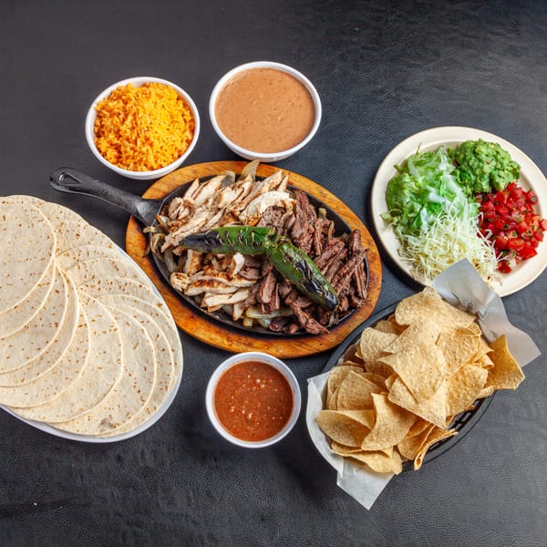 Dona Mary's sizzling chicken and beef fajitas with rice, beans, tortillas, chips, salsa, and toppings.