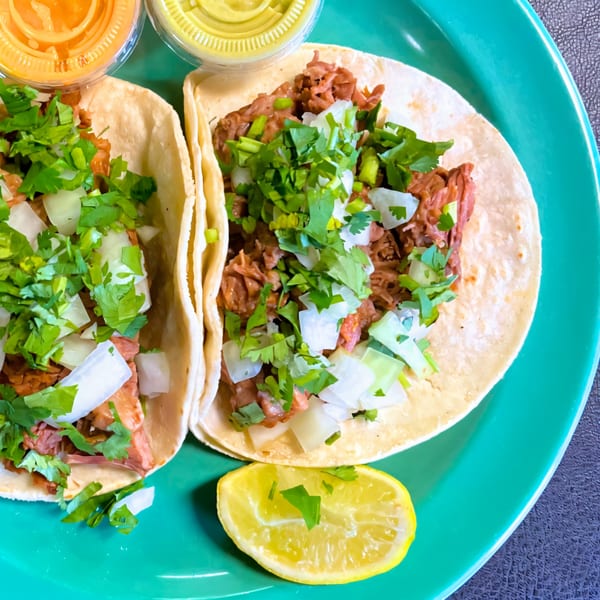 Two Dona Mary Mexican tacos with meat, cilantro, onions, and lime on a green plate with sauces.