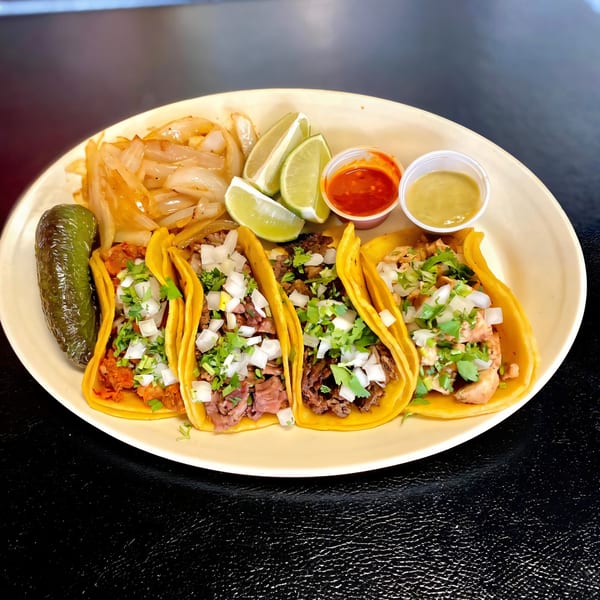 Four Dona Mary tacos with various fillings, cilantro, onions, limes, sauces, grilled onions, and a jalapeño.