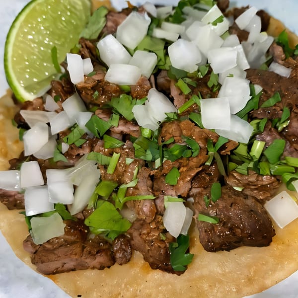 Close-up of a Dona Mary carne asada taco with diced onions, cilantro, and a lime wedge.