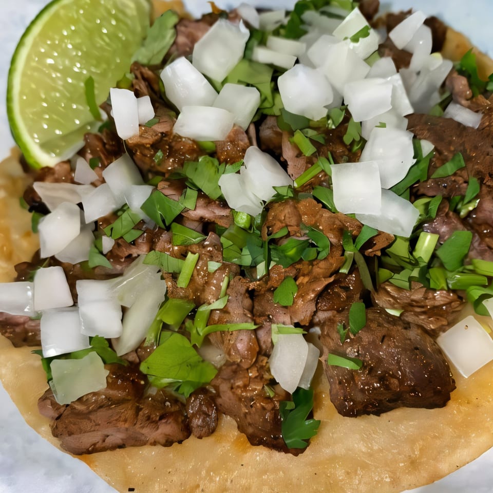 Close-up of a Dona Mary carne asada taco with diced onions, cilantro, and a lime wedge.