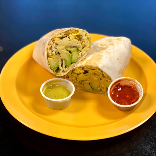 Two Dona Mary burritos, one cut open to show avocado and scrambled eggs, with green and red salsa.